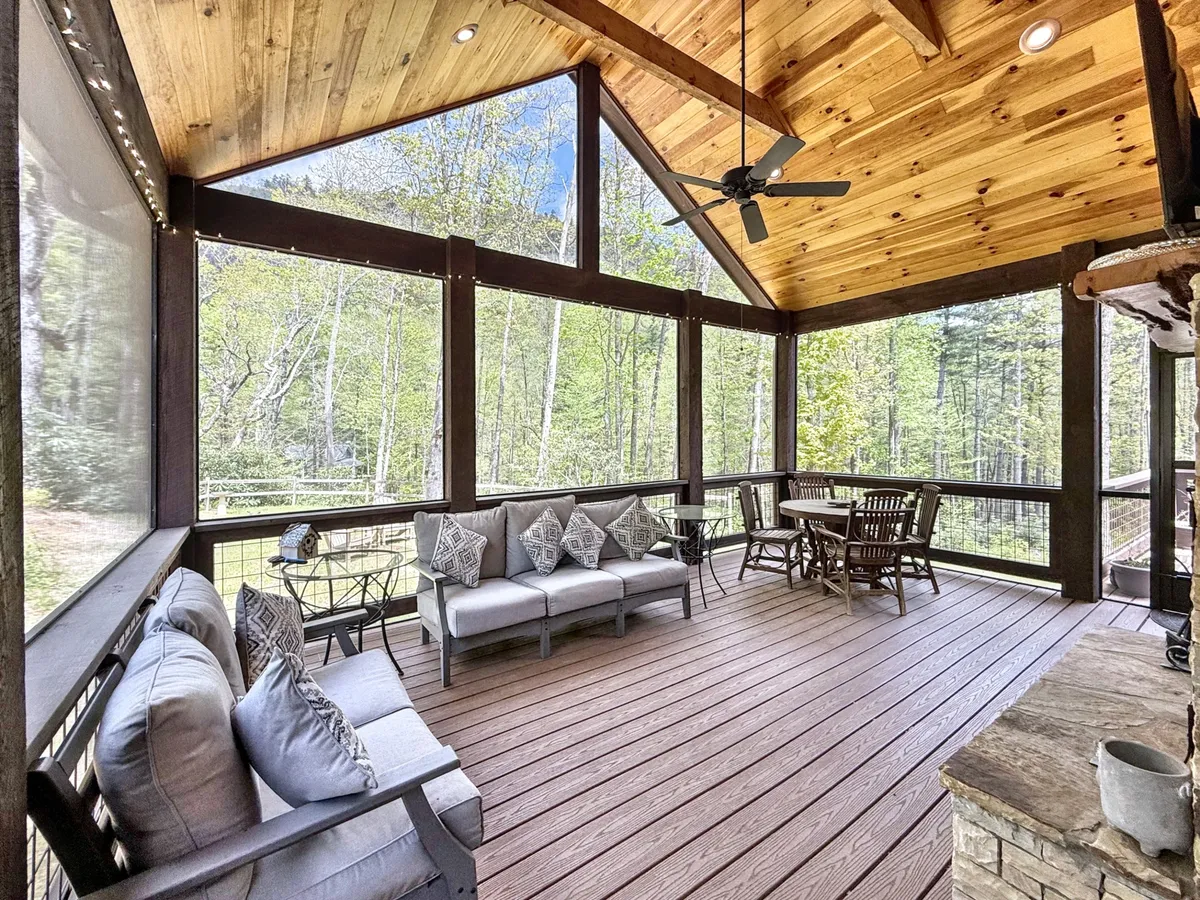 A cozy interior seating area with large windows offers panoramic views of the surrounding forest. The dining table for four and comfortable chairs invite guests to relax and take in the natural scenery, blurring the boundary between indoors and outdoors.