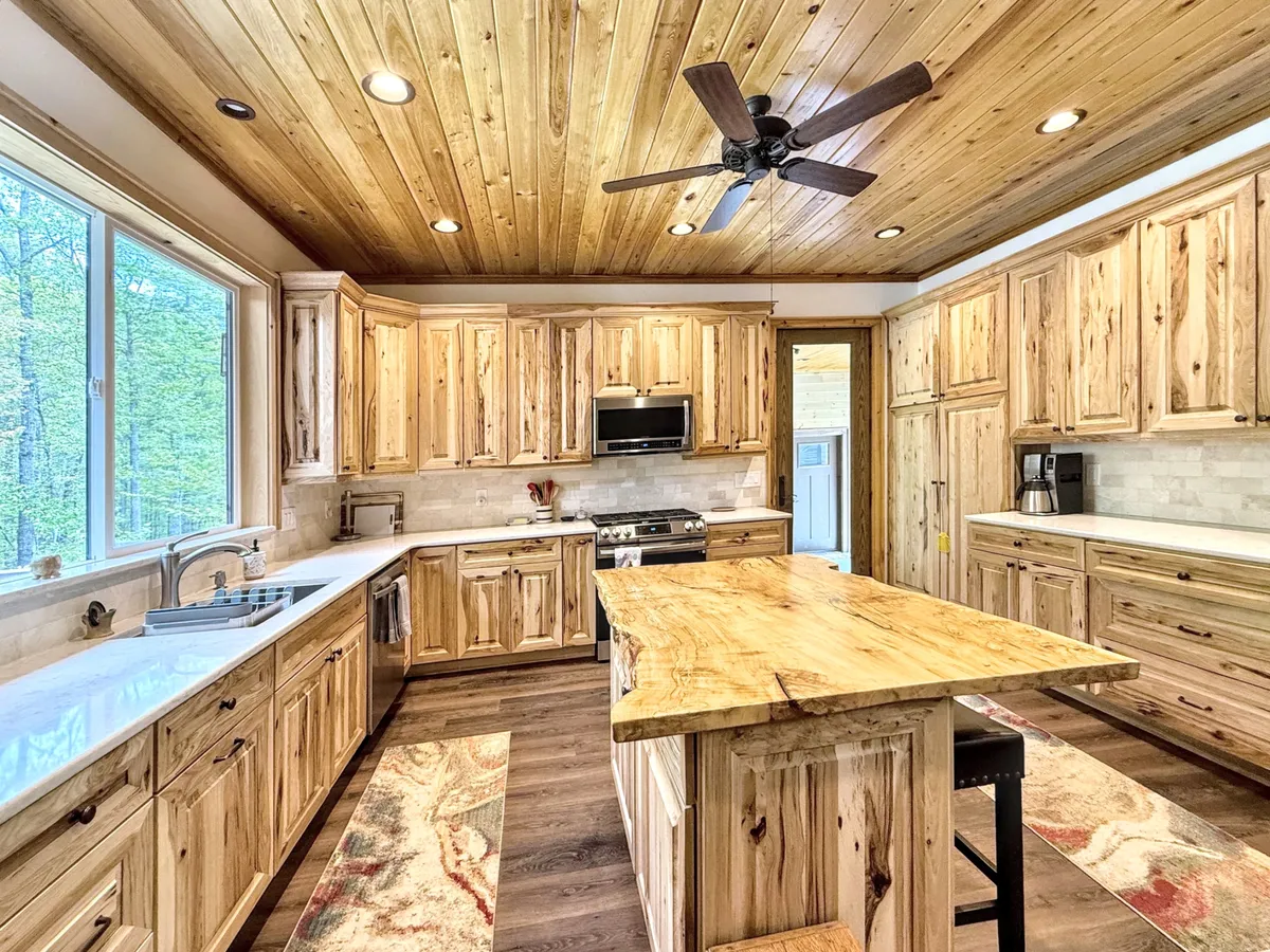 A spacious kitchen featuring a large wooden island, natural wood cabinetry, and expansive windows looking out to a lush green woodland. The scene feels warm and inviting, with generous counter space and modern appliances visible. The view out the windows emphasizes a connection to the outdoors, enhancing the sense of tranquility and inspiration in the kitchen.