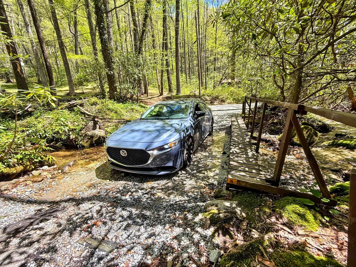 A car parked near a rustic wooden bridge, with a stream, dense trees, and a sense of discovery in the air. The scene evokes the spirit of exploration, with opportunities for hiking, scenic drives, and spontaneous nature adventures.