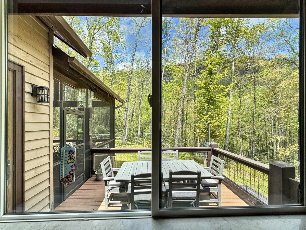 An inviting screened deck with a wooden dining table, surrounded by trees. The outdoor space is bathed in natural light and offers a tranquil setting for alfresco dining, seamlessly connecting the indoors to the woodland exterior.