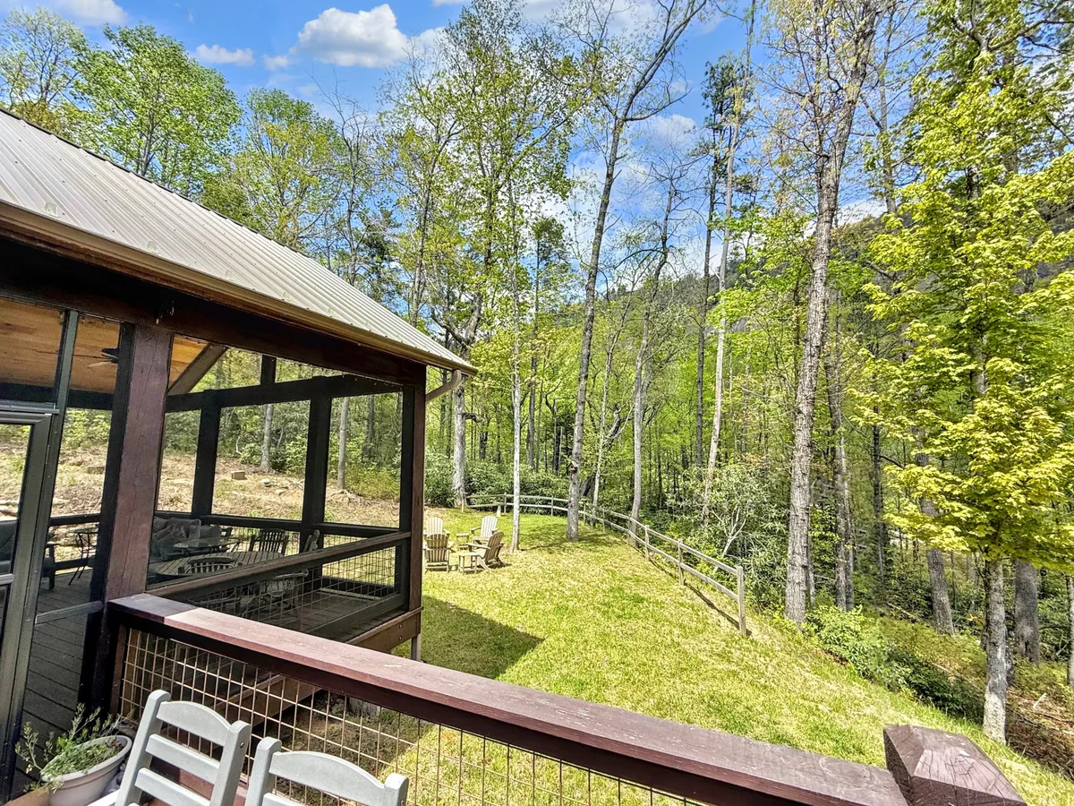 A tranquil wooden deck with adjoining chairs overlooks a backdrop of lush greenery and distant trees. The serene setting is ideal for relaxing, gathering with friends, or enjoying the sights and sounds of nature. The layout and placement of furniture foster a cozy, communal atmosphere.