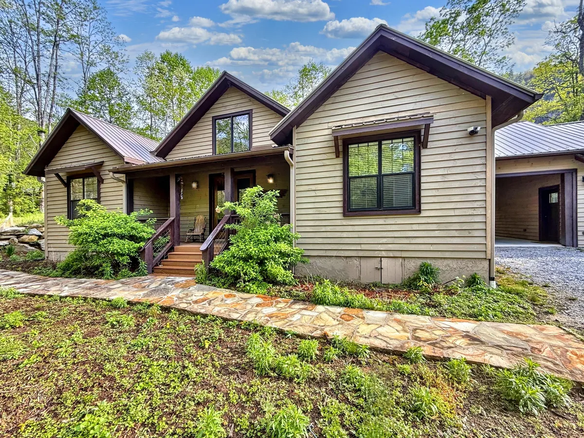 A welcoming front porch overlooks a landscaped garden, with a winding stone pathway leading to the entrance. The gabled roof and inviting outdoor seating evoke a sense of small-town charm and relaxation, while the scene hints at morning coffee rituals and evening gatherings.