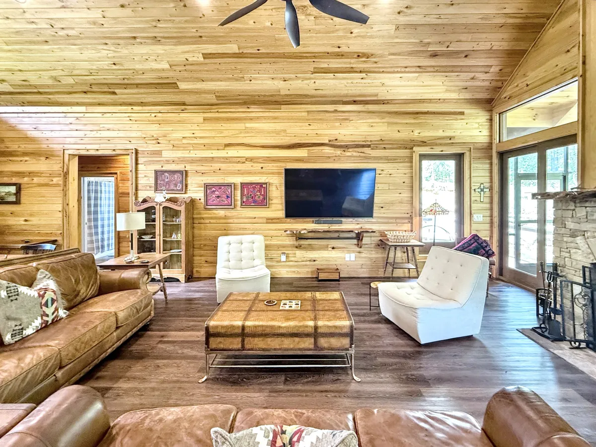 A view of a living area with a plush leather sofa, coffee table, TV, and warm wooden walls. The space feels intimate and perfect for game nights, movie marathons, or relaxed conversations by the fire.